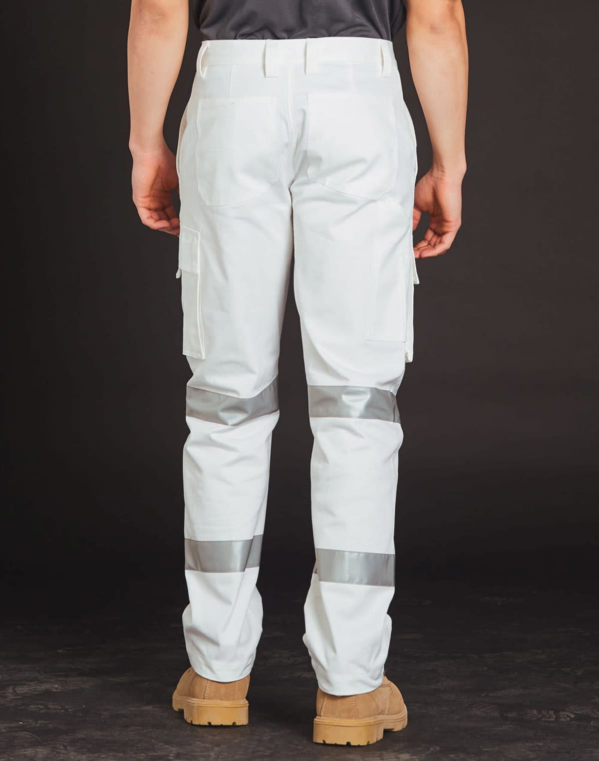 A person wearing white cargo pants with reflective stripes and tan work boots is standing with their back facing the camera against a dark background.
