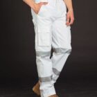 A person wearing white cargo work pants with reflective stripes and tan work boots. The background is black, highlighting the details of the pants, which include pockets on the side. The persons hands are in their pockets.