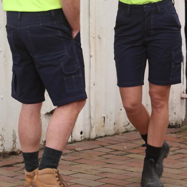 Two people in bright yellow shirts and dark cargo shorts stand on a brick sidewalk. One has brown boots with socks, and the other wears black boots with black socks. They face each other, with a white wall in the background.