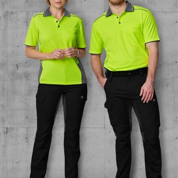 Two people stand side by side wearing matching outfits: neon green polo shirts with gray collars and black pants. They have brown shoes and are in front of a gray, concrete-like background.