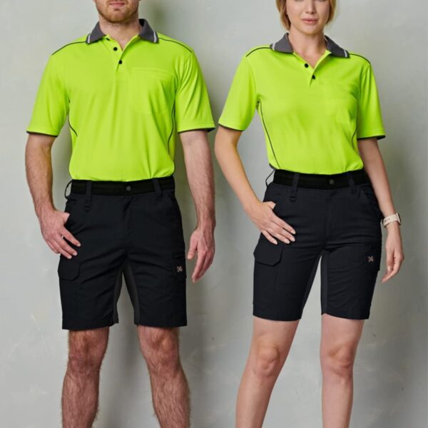 A man and a woman stand side by side against a plain background, wearing matching neon green polo shirts and black shorts. Both are wearing brown work boots.
