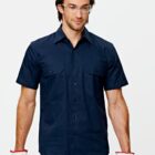 A person wearing safety glasses and a navy blue short-sleeve button-up shirt holds work gloves. They have a neutral expression and are standing against a plain background.