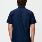 A person with medium-length brown hair is facing away from the camera, wearing a dark blue short-sleeve button-up shirt. The background is plain white.