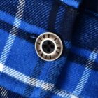 Close-up of a blue and black plaid fabric with a button attached. The button has four holes and lettering around its edge. The pattern consists of intersecting stripes in varying shades of blue, black, and white.
