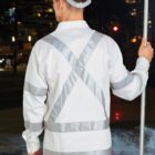 A construction worker wearing a white uniform with reflective stripes holds a stop sign. They are standing on a street at night, with blurred lights of buildings and cars in the background.