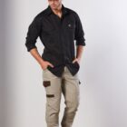 A man wearing a black cap, a black long-sleeve shirt, and beige cargo pants with pockets poses against a white background. He is looking down with his hands in his pockets.