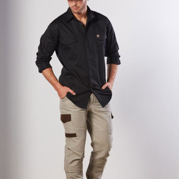 A person wearing a black cap, long-sleeve black shirt, beige cargo pants, and black boots stands against a plain white background. They have their hands in their pockets and are looking down.