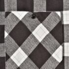 Close-up of a black and white checkered flannel fabric with a buttoned pocket. The pattern features large squares in alternating shades, typical of a plaid design.