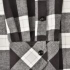 Close-up of a black and white plaid fabric with a detailed view of a shirt cuff. The cuff is fastened with two black buttons. The pattern consists of intersecting lines forming a checkered design.
