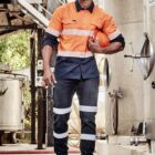 Man in high-vis workwear holding orange hard hat, standing at an industrial site.