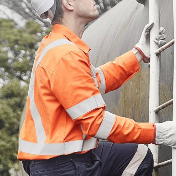 A construction worker wearing an orange safety jacket, white hard hat, and gloves climbs a metal ladder outdoors. He looks upward, next to a large industrial pipe, with trees in the background.