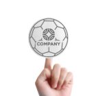 Hand holding a circular sticker with a soccer ball design and the word COMPANY in the center against a white background.