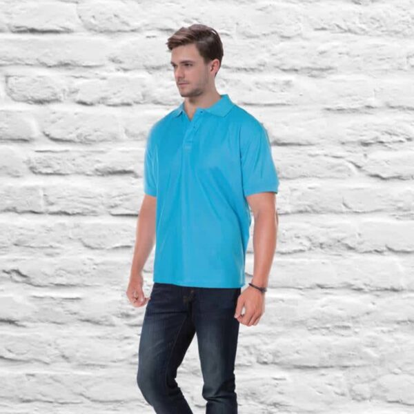 Wearing the AERO POLO in vibrant blue and dark jeans, a man stands against a white brick backdrop. He gazes to the side, with one hand in his pocket as he steps slightly forward.