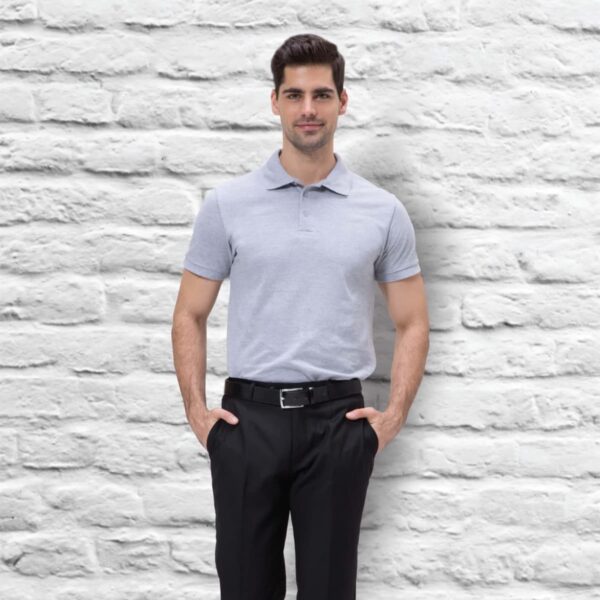 A man wearing a Euro POLO in light gray and black pants stands with hands in pockets against a white brick wall. He has dark hair and a slight smile.