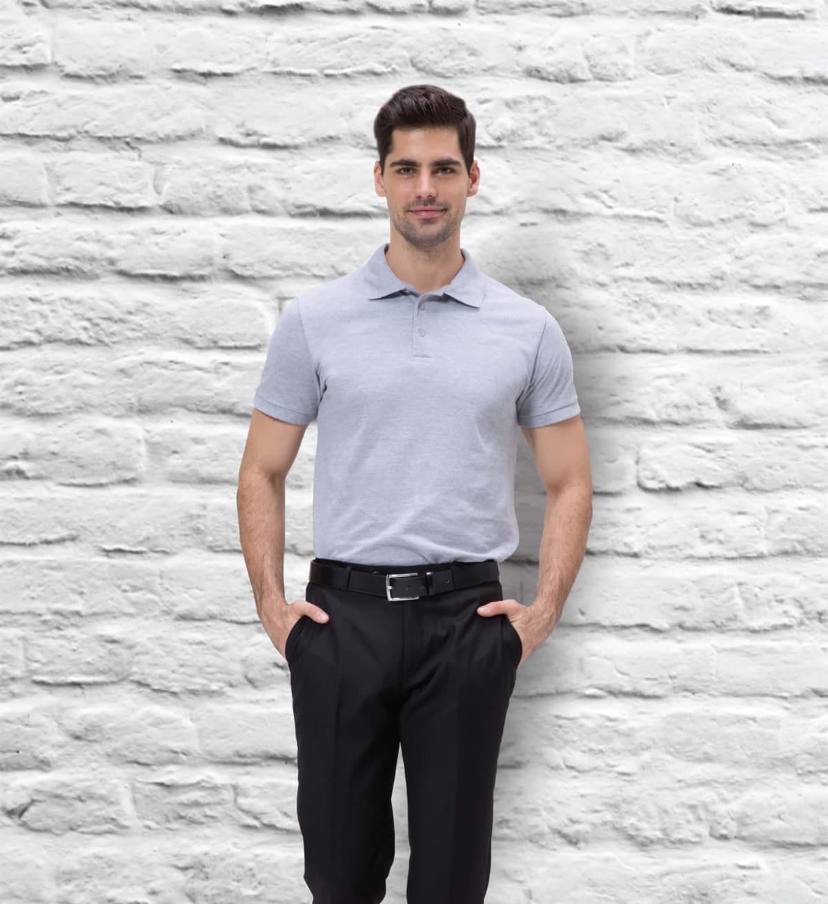 A man wearing a Euro POLO in light gray and black pants stands with hands in pockets against a white brick wall. He has dark hair and a slight smile.