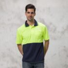A man in a Burst Polo, featuring a neon yellow and navy color-block design, stands against a light gray background. He has short dark hair and is dressed in jeans.
