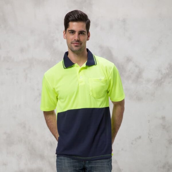 A man in a Burst Polo, featuring a neon yellow and navy color-block design, stands against a light gray background. He has short dark hair and is dressed in jeans.