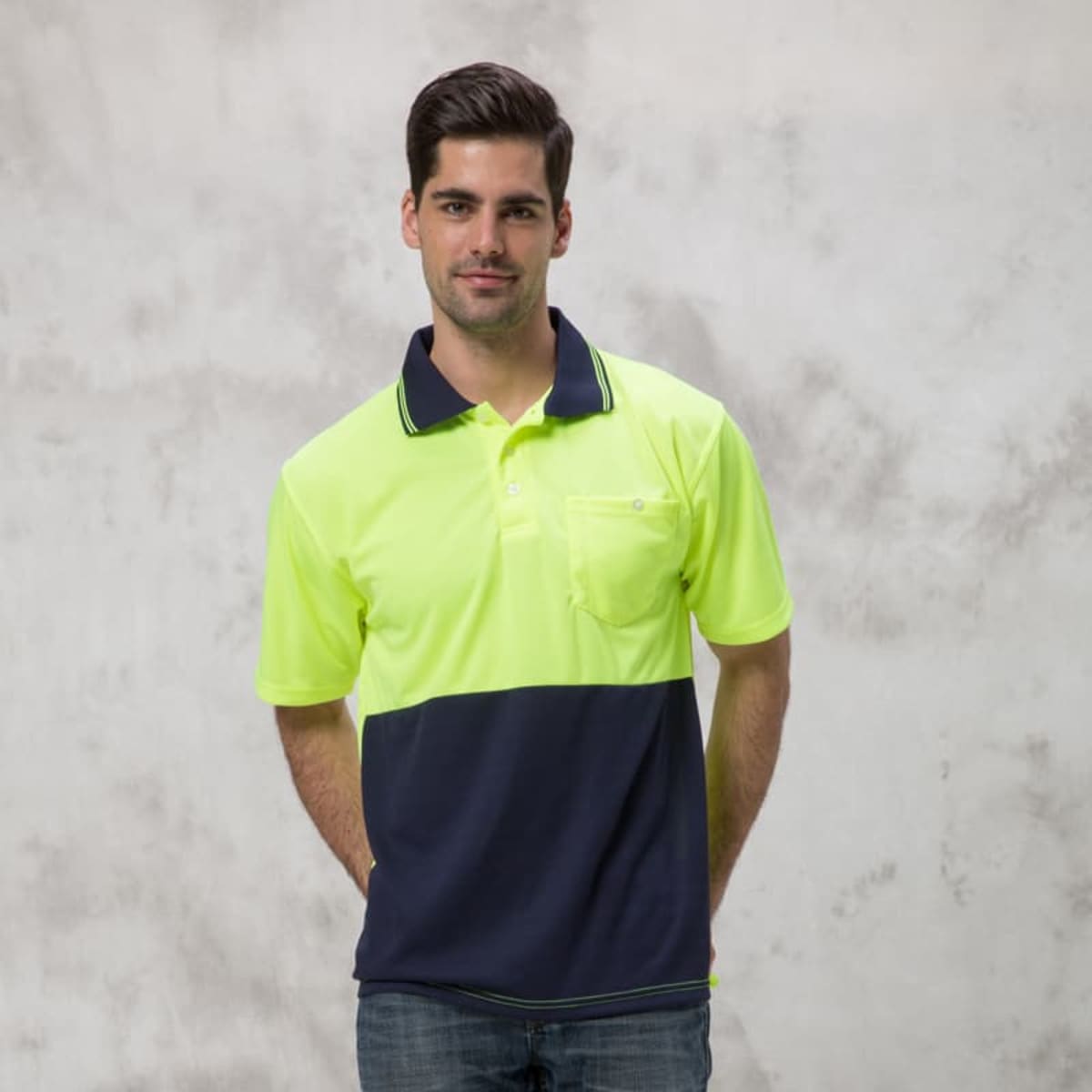 A man in a Burst Polo, featuring a neon yellow and navy color-block design, stands against a light gray background. He has short dark hair and is dressed in jeans.