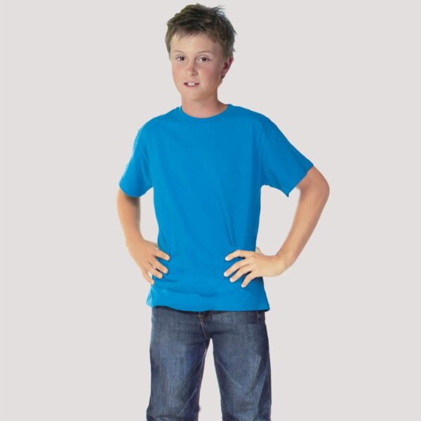 A boy stands confidently with hands on hips, wearing a bright blue Tide JUNIOR TEE and jeans, against a neutral background.