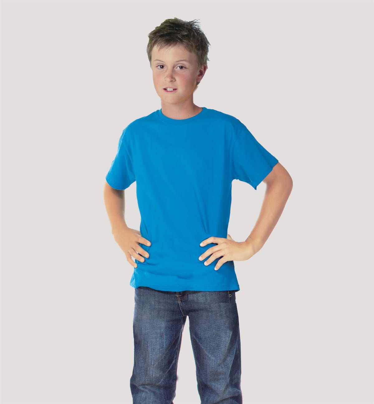 A boy stands confidently with hands on hips, wearing a bright blue Tide JUNIOR TEE and jeans, against a neutral background.