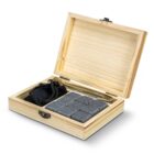 Open wooden box with whiskey stones, metal tongs, and a small black pouch inside.