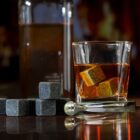 A glass of whiskey with whiskey stones, tongs, and a bottle in the background.