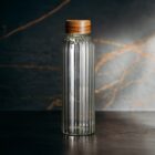 A clear glass bottle with vertical ridges and a wooden cap on a dark surface.