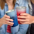 Two people clink blue and red cups together, both wearing casual clothes.