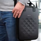 Person holding a black textured Rollink laptop case while wearing jeans and a gray sweater.