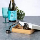 Wine opener set with corkscrew, wine bottle, and blue glass on a gray surface.
