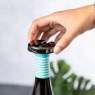 Hand placing a black wine stopper on a bottle with blue and white stripes on the neck.