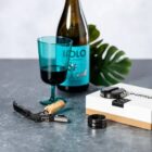 A wine bottle, blue glass, corkscrew, and box on a gray surface with a green leaf.