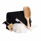 Black toiletry bag with a wooden hairbrush, toothbrush, white loofah, and a labeled tag.