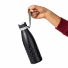 A hand holds a black reusable water bottle by its strap against a white background.