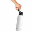A hand holds a white water bottle by its black cap handle.