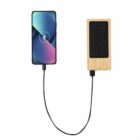 A smartphone is charging, connected by cable to a wooden solar power bank.