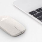 Minimalist white wireless mouse next to a silver laptop on a white surface.