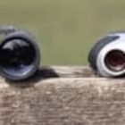 Three pairs of binoculars are lined up on a wooden surface against a blurred green background.