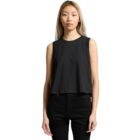 Woman in a sleeveless black top and black jeans standing against a white background.
