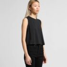 Woman in a black sleeveless top and black pants standing against a plain light background.