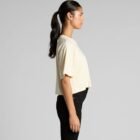 Woman in a light yellow top and black pants standing in profile against a gray background.