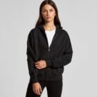 Woman in black zip-up hoodie and white shirt standing against a plain gray background.