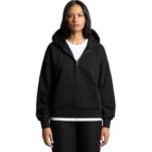 Woman wearing a black hoodie over a white t-shirt, standing against a white background.