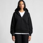 Woman in a black hoodie and white T-shirt standing against a plain light background.