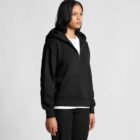 Woman in a black hoodie and pants standing against a plain light gray background.