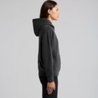 Woman in a black hoodie and black pants standing in profile against a plain background.
