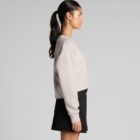 Woman in a beige sweatshirt and black skirt standing in profile against a gray background.