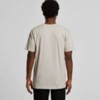 Man standing with his back to the camera, wearing a plain beige t-shirt and black pants.