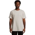 Man wearing a plain beige t-shirt and black pants, standing against a white background.