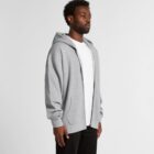 Man wearing a gray zip-up hoodie over a white shirt and black pants, standing sideways.